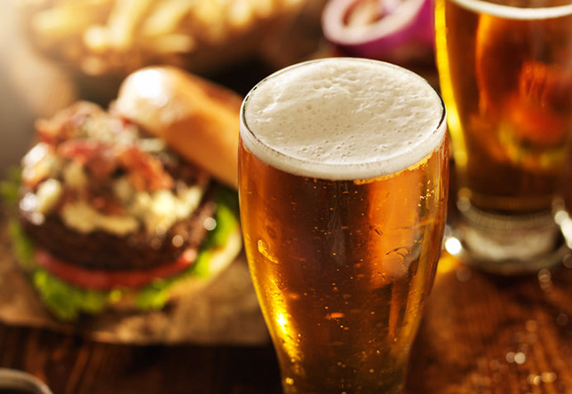 A beer on a table with food in the background