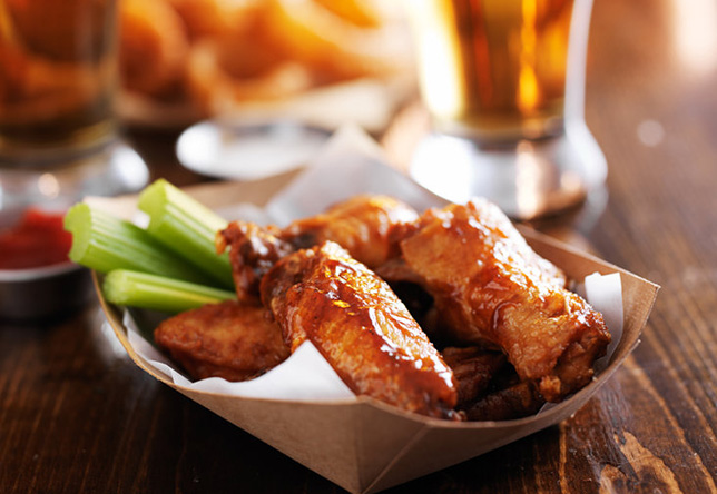 A basket of wings with celery and a beer in the background
